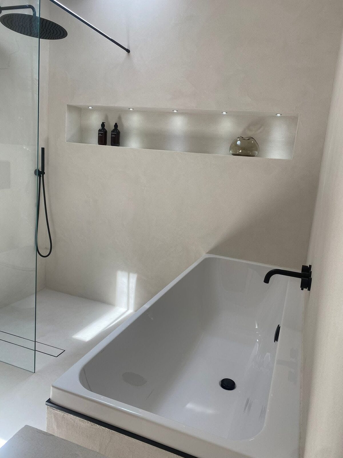 Finished cream microcement bathroom with bath and lit niche
