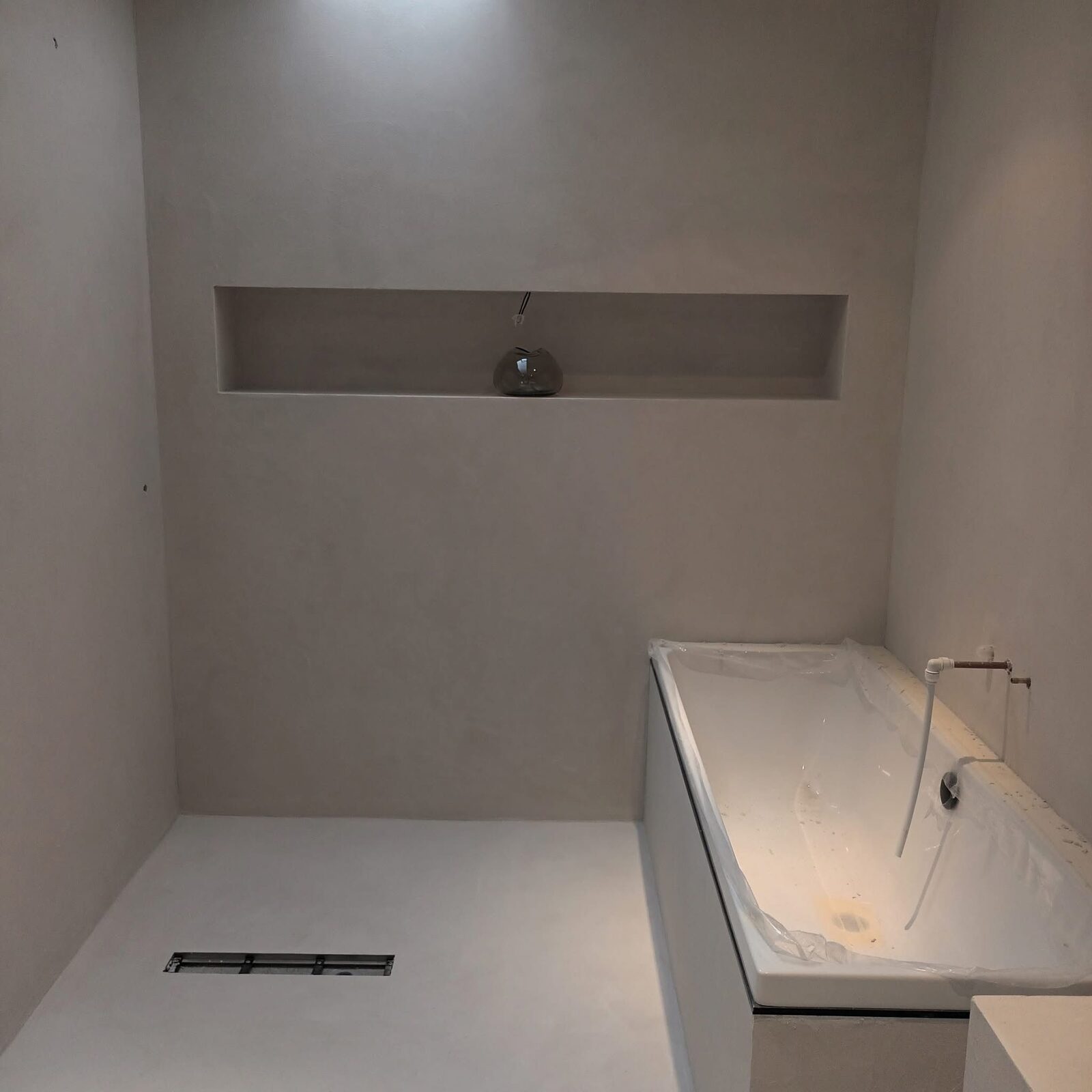 Finished grey microcement bathroom with bath and niche